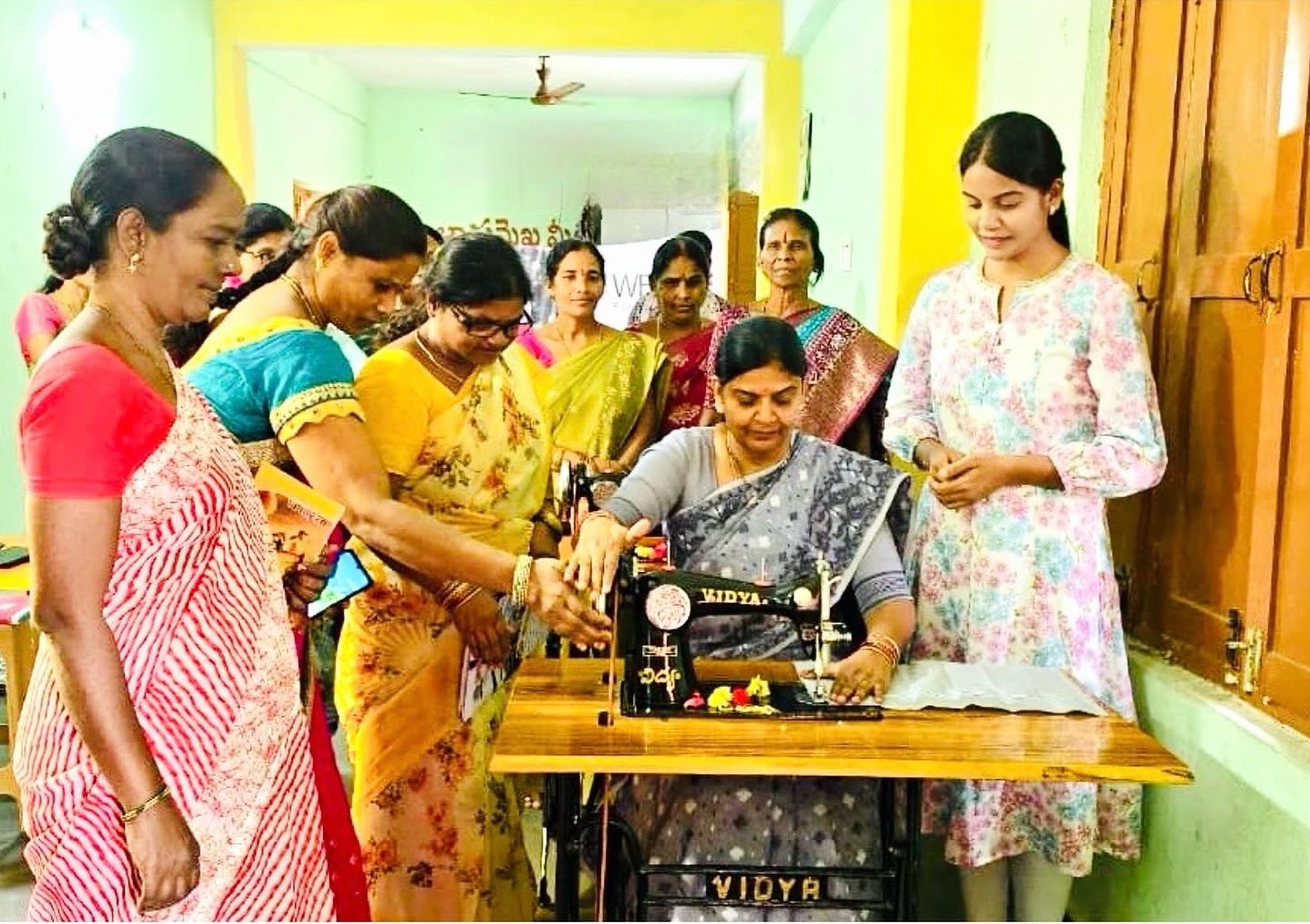 Women gathered around a sewing machine on opening day at the We & She skill centre