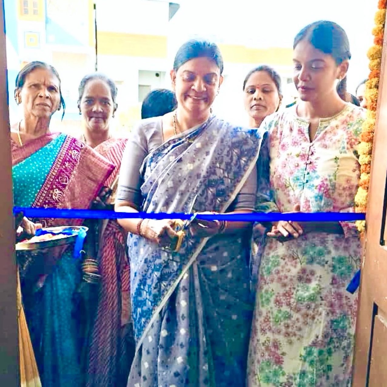 The chief guest cuts a blue ribbon to open the skill centre as the founder and local women look on