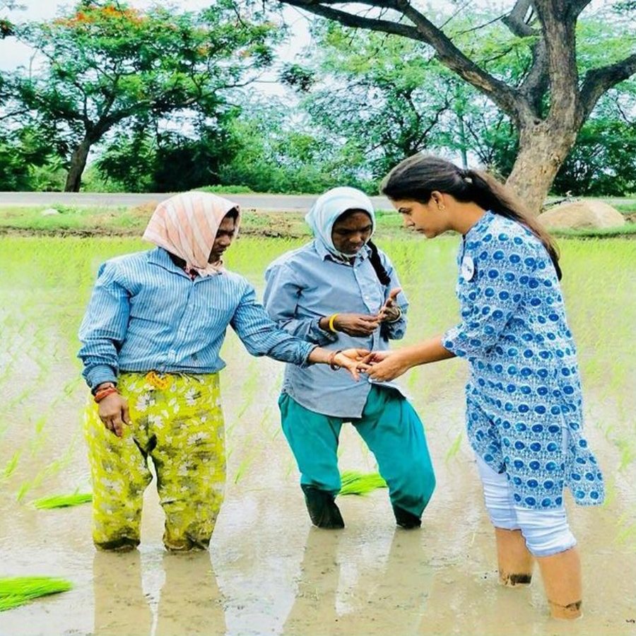 The founder standing in a flooded paddy field talking with women farm workers